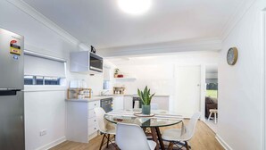 A modern kitchen with white cabinets, a digital inverter refrigerator, and a glass dining table with white chairs. - Bright, Cosy and Central Cottage- Free Wi-fi, Netflix and Disney Plus (Orange)