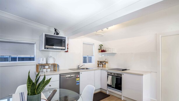 A modern kitchen with white cabinets, a built-in microwave, a dishwasher, and an oven. - Bright, Cosy and Central Cottage- Free Wi-fi, Netflix and Disney Plus (Orange)