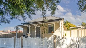 A two-story house with a porch, a mailbox, and a picket fence. - Bright, Cosy and Central Cottage- Free Wi-fi, Netflix and Disney Plus (Orange)