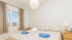 Habitación de hotel con una cama grande, dos mesitas de noche, una ventana con cortinas y una lámpara colgante.