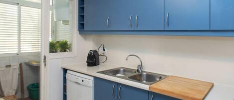 Una cocina compacta con armarios azules, un lavavajillas, un fregadero y una estufa.