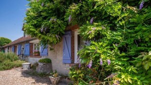 A rustic house with a gravel driveway, a stone planter, and lush greenery.