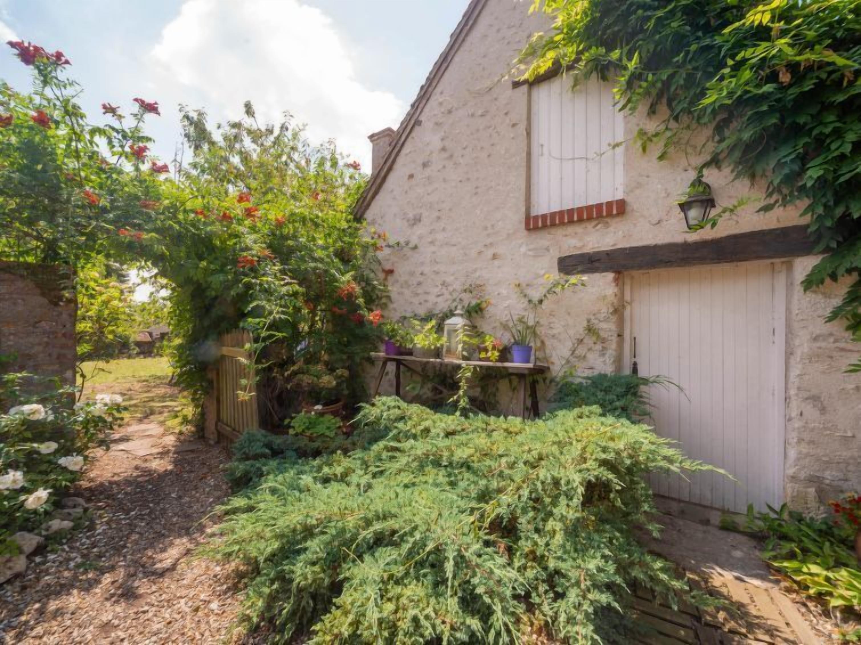 Une maison de campagne en pierre, avec un sentier de jardin menant à une porte blanche.