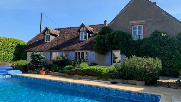 A house with a swimming pool, surrounded by greenery and a clear sky.