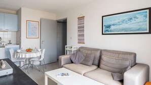 Ett modernt vardagsrum med en beige soffa, ett vitt soffbord och en matplats med ett vitt bord och stolar.