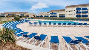 Ett poolområde med solstolar placerade i en halvcirkel runt en central pool, omgivet av flervåningsbyggnader med balkonger.