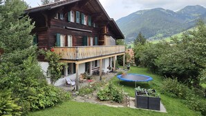 A wooden chalet with a balcony, surrounded by lush greenery and mountains in the background. - Hübeli (Kopp) by Interhome (Zweisimmen)