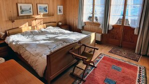 A wooden-paneled bedroom with a bed, a nightstand, a chair, and a window with curtains. - Hübeli (Kopp) by Interhome (Zweisimmen)