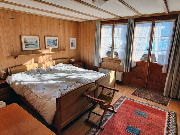 A wooden-paneled bedroom with a bed, a nightstand, a chair, and a window with curtains.