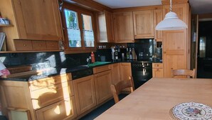 A kitchen with wooden cabinets, a black countertop, a stove, and a dining table with chairs. - Hübeli (Kopp) by Interhome (Zweisimmen)