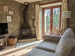 Ein gemütliches Wohnzimmer mit Steinwand, Kamin, Fernseher, einer Couch und einem mit Vorhängen drapierten Fenster.