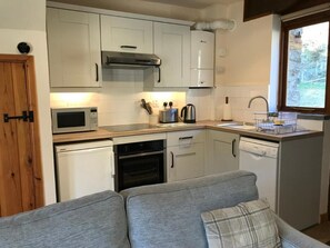 A compact kitchen with white cabinets, a microwave, a kettle, and a dishwasher. - The Coach House - Secluded Cottage - Cardigan Bay - Sleeps 2 (Cardigan)