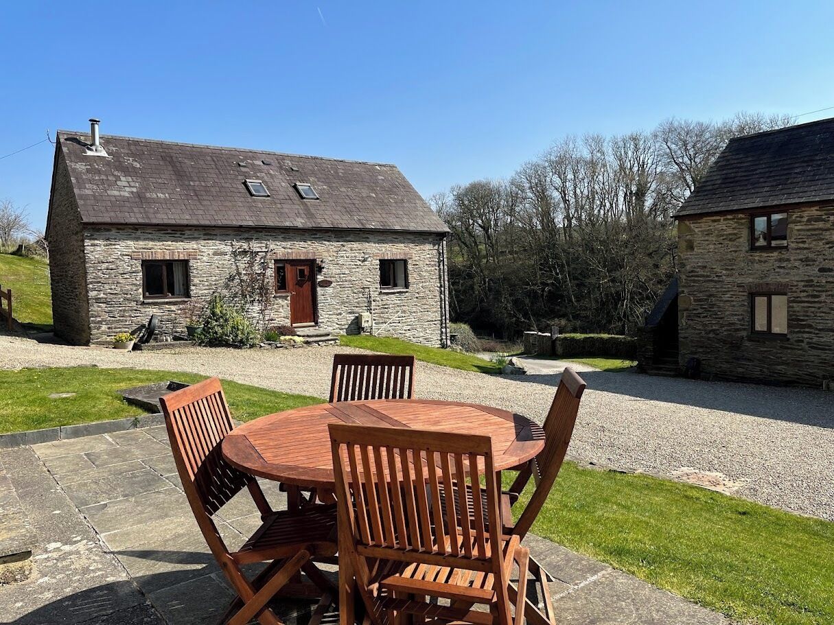A stone building with a wooden table and chairs in the foreground.