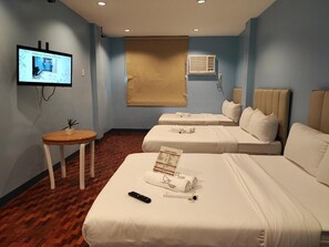 Ein Hotelzimmer mit zwei Betten, einem Fernseher, einem kleinen Tisch und einem Fenster mit Jalousie.