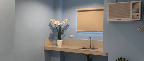 A bathroom with a sink, a mirror, a window with blinds, and a wall-mounted air conditioner.