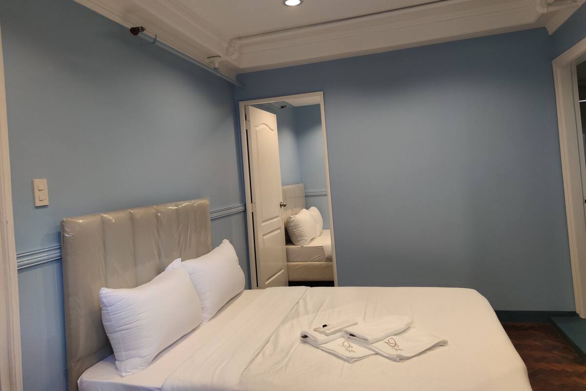 Un lit bien fait, avec du linge de lit et des serviettes blancs, une tête de lit blanche et un mur bleu.