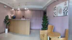 A reception area with a wooden desk, two chairs, a potted plant, and a wall with abstract art. - Glory Hotel Cubao (Quezon City)