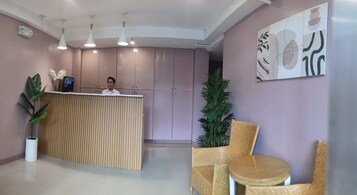 A reception area with a wooden desk, two chairs, a potted plant, and a wall with abstract art.
