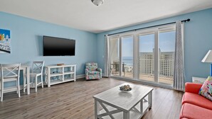 A living room with a TV, a coffee table, a sofa, and a balcony with a view of the ocean. - Laketown Wharf 913 (Panama City Beach)