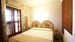 Une chambre à coucher comprenant un lit, un climatiseur, une fenêtre avec des volets, une table de chevet et une armoire.