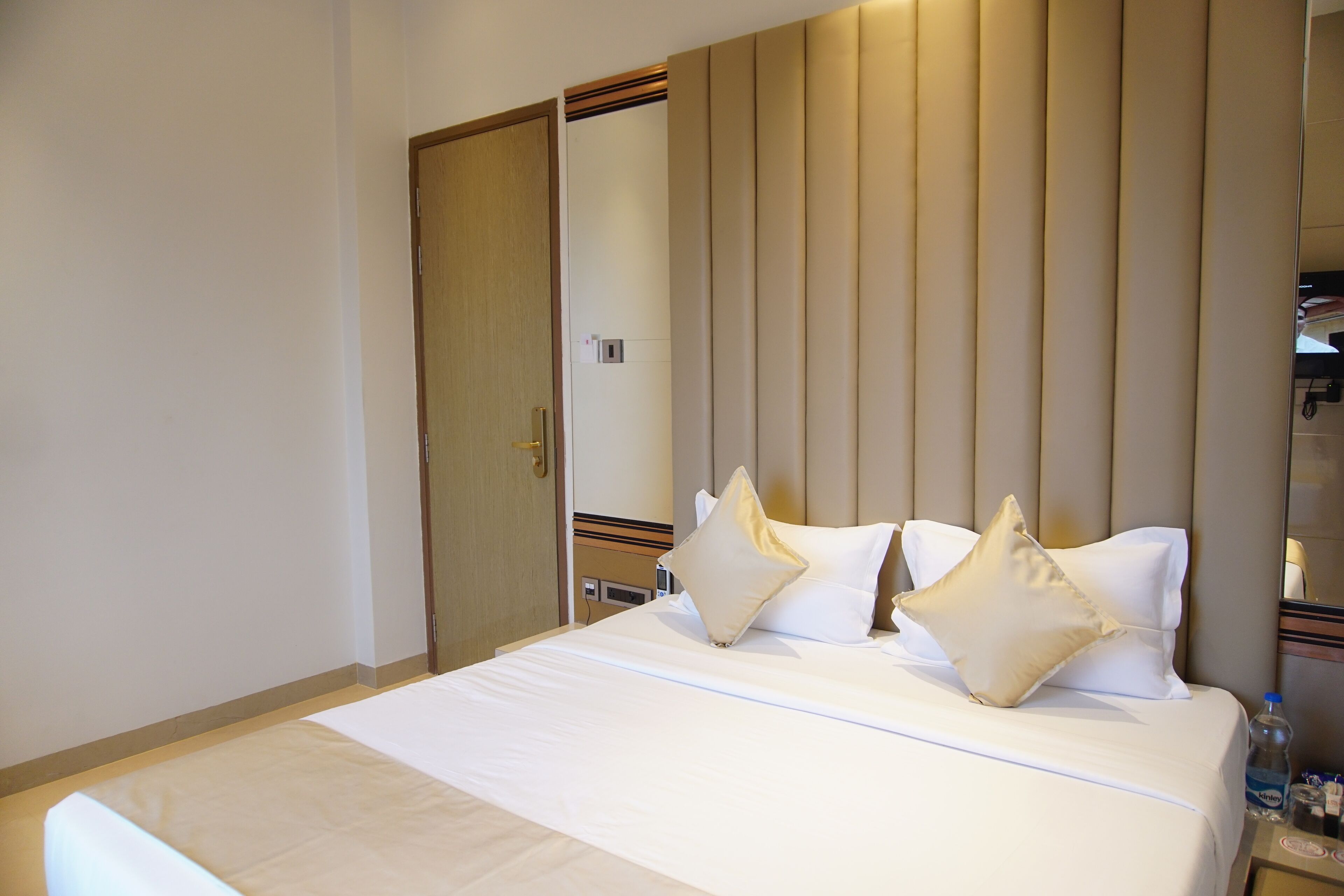 A hotel room with a large bed, two pillows, a bedside table with a bottle, and a mirror on the wall.