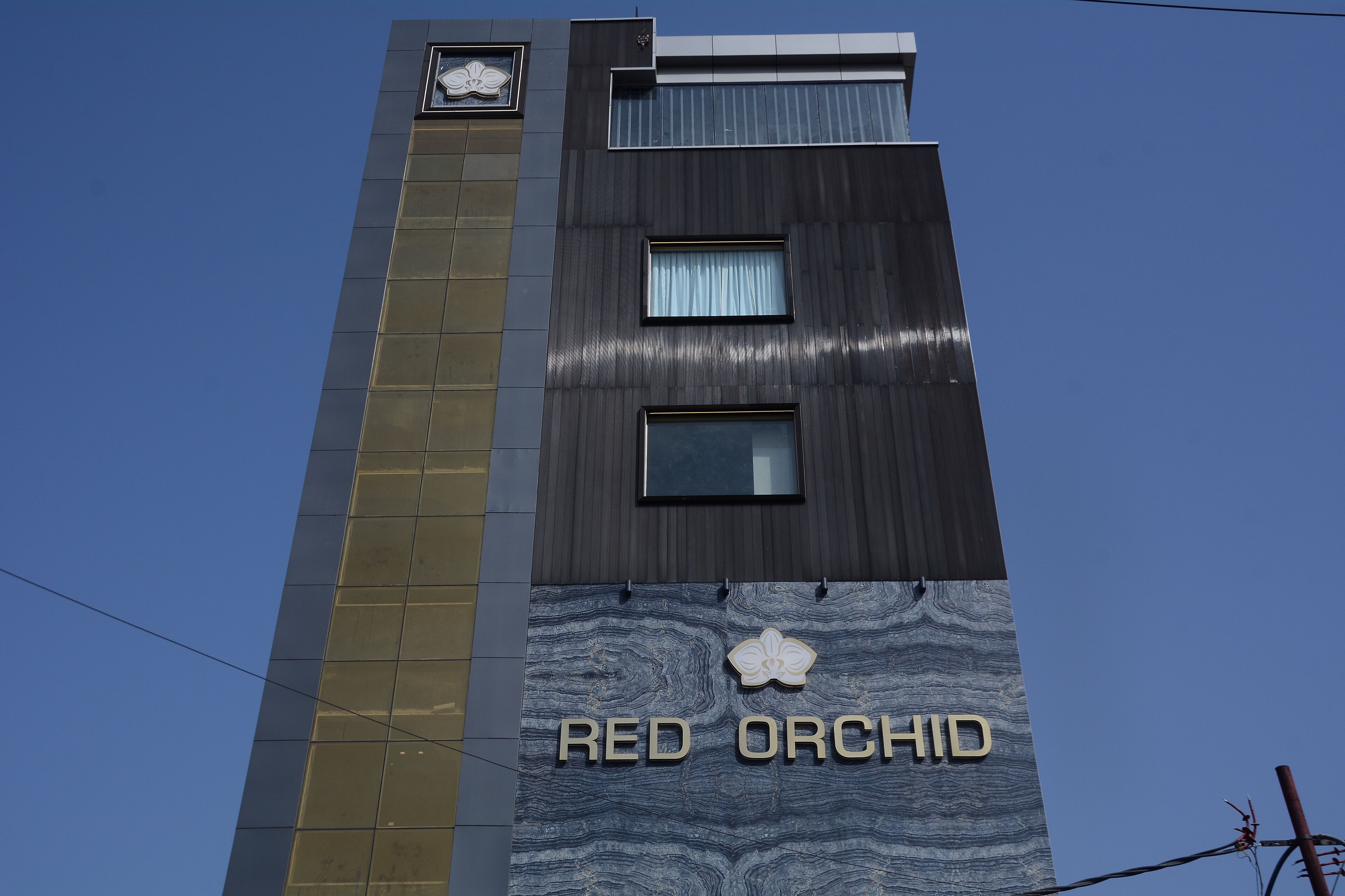 Un edificio con el letrero 'RED ORCHID', diseño moderno con una franja vertical dorada y fachada texturizada.