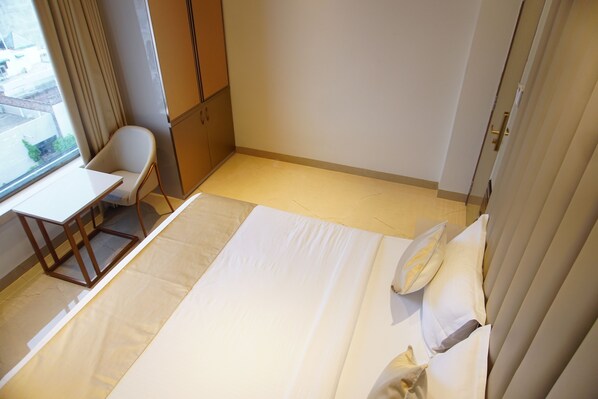 A hotel room with a bed, a chair, a small table, and a window with curtains.
