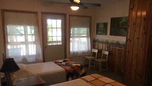 A room with two beds, a ceiling fan, a desk with a lamp, and a chair. - Felker's Cottage: Fall Color Getaway | Lakefront Cottage Near Tunnel of Trees (Vanderbilt)