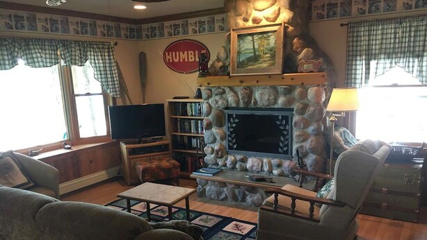 A cozy living room with a stone fireplace, a television, and a bookshelf. - Felker's Cottage: Fall Color Getaway | Lakefront Cottage Near Tunnel of Trees (Vanderbilt)