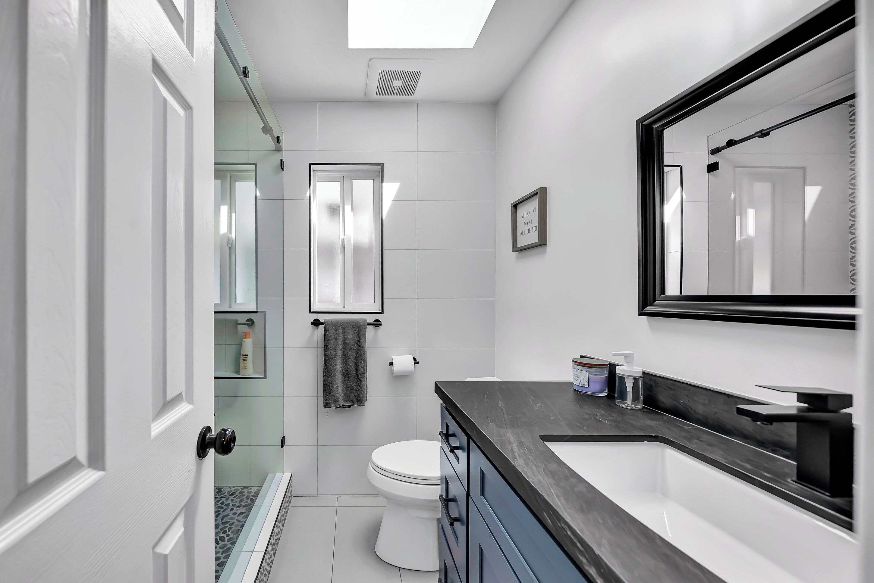 A modern bathroom with a glass shower enclosure, a white toilet, a black countertop with a sink, and a large mirror.
