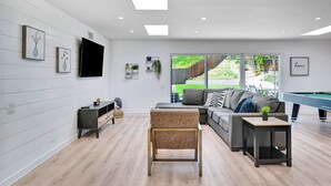 Una sala de estar moderna con un sofá, una mesa de centro, una mesa de billar y un televisor montado en la pared.