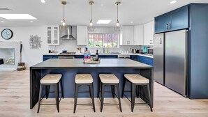 Una cocina moderna con una isla central, taburetes de bar, luces colgantes y un refrigerador grande.