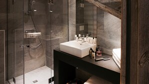 Uma casa de banho moderna com cabine de duche em vidro, lavatório branco com produtos de higiene e toucador de madeira.