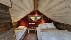 Um quarto de sótão aconchegante com duas camas, uma mesa pequena e uma janela.