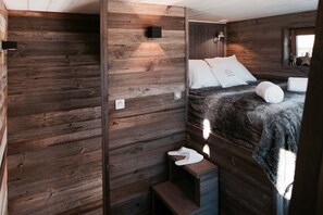 A rustic wooden room with a bed, a bench, and a small table.