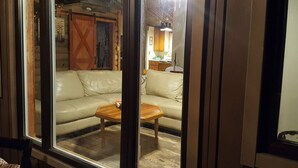 A living room with a sofa and a coffee table, wooden flooring, and a kitchen area in the background. - On the Riverbend Cabin (Claxton)