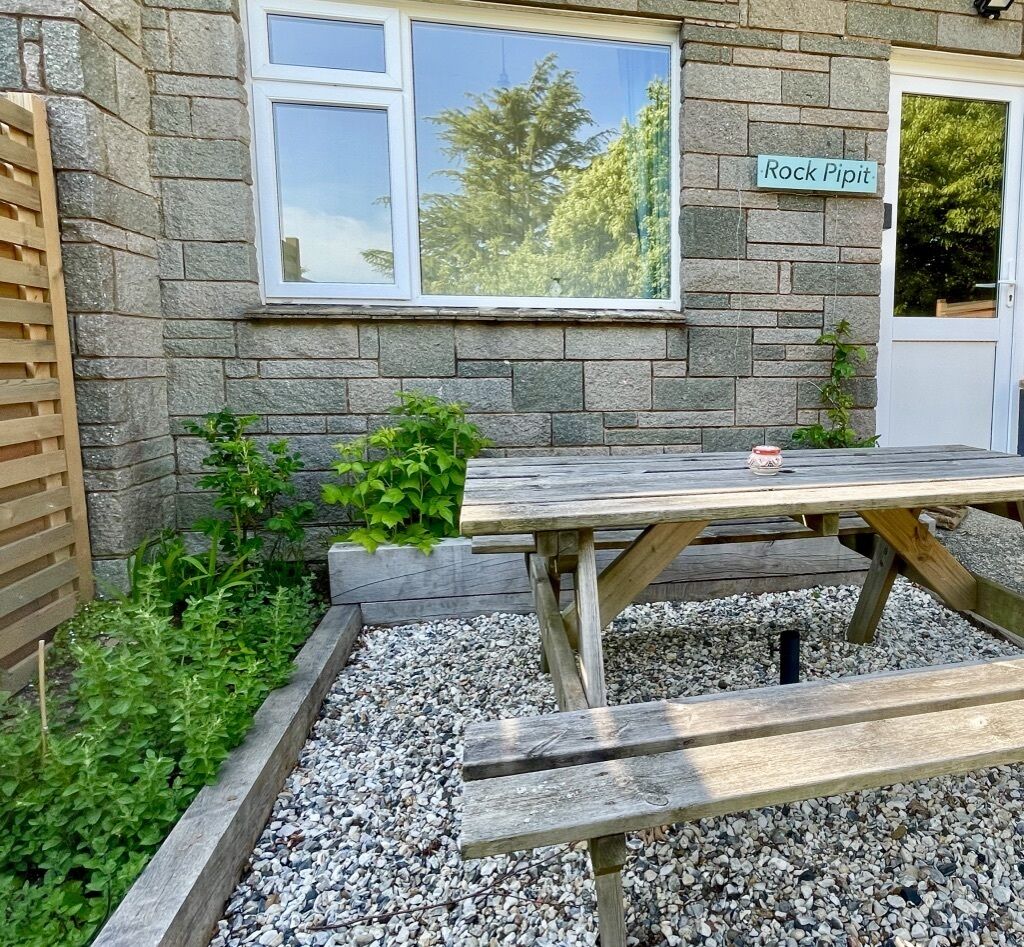 A stone building with a wooden picnic table and a sign reading "Rock Pipit".