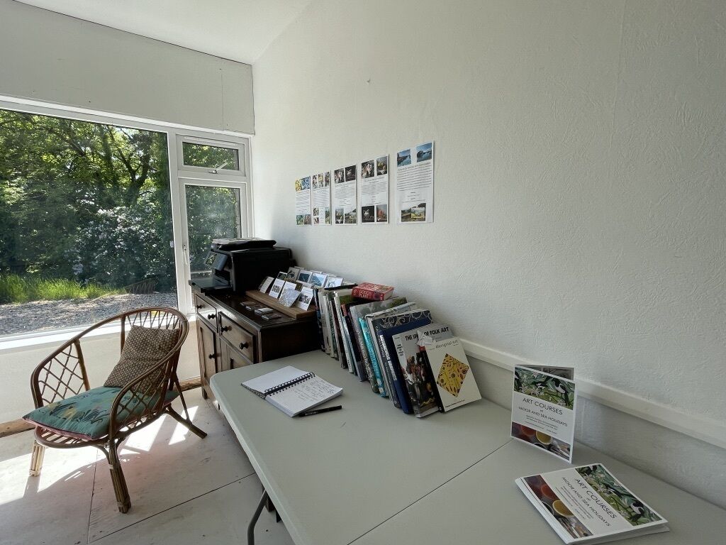 A room with a desk, chair, and books. There is a window with a view of trees.