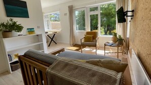 Une chambre moderne avec un grand lit, une chaise en bois, une petite table et un téléviseur fixé au mur.