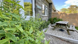 Une maison avec une façade en pierre, une clôture en bois et un jardin aménagé avec du gravier, comprenant une table et un banc en bois.