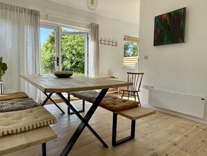 A modern dining area with a wooden table and benches, a view through a glass door, and a wall-mounted abstract painting.