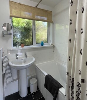 A bathroom with a sink, mirror, window with frosted glass, and a bathtub.