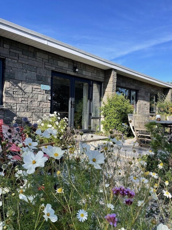 A stone building with a glass door entrance, surrounded by a garden with various flowers.