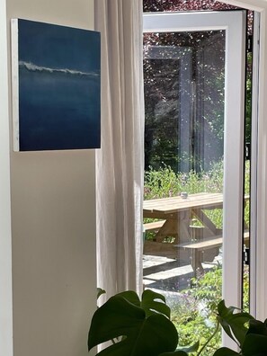 A room with a view of a garden through a glass door, a wooden bench outside, and a painting on the wall. - Whitebeam Cottage, Moor and Sea, beautiful views of Exmoor (Lynton)