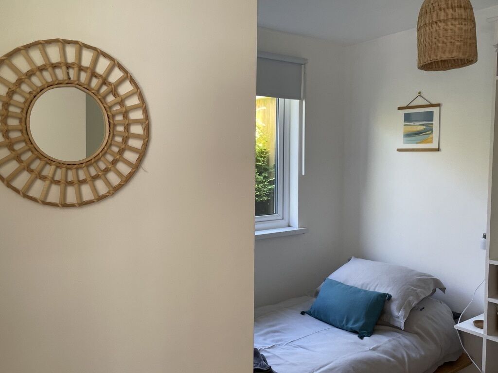 A bedroom with a bed, a window, a wall-mounted mirror, and a hanging light fixture.