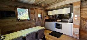 A compact kitchen with wooden walls, a dining area, and a window with a view of greenery.