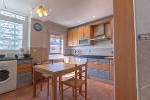 A compact kitchen with wooden cabinets, a microwave, a sink, and a dining table with chairs.