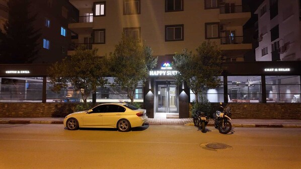 Entrada de hotel con un letrero que dice "HAPPY SUIT" y un coche estacionado en la parte delantera.