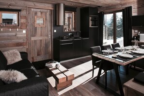 Une cuisine moderne avec des meubles de couleur sombre, une hotte en acier inoxydable et un coin repas doté d’une table en bois, mise pour six personnes.