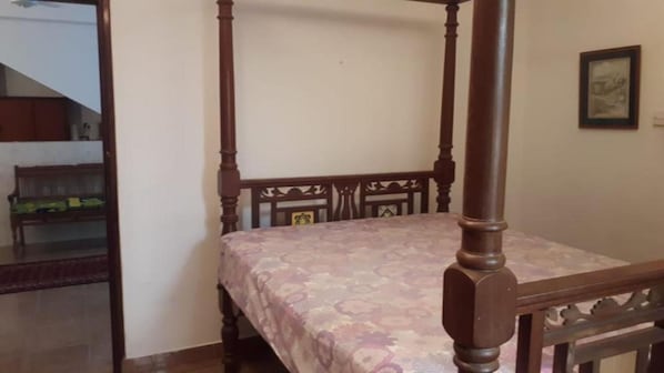 Una cama con dosel y una colcha estampada floral en una habitación con un banco de madera y un cuadro enmarcado en la pared.